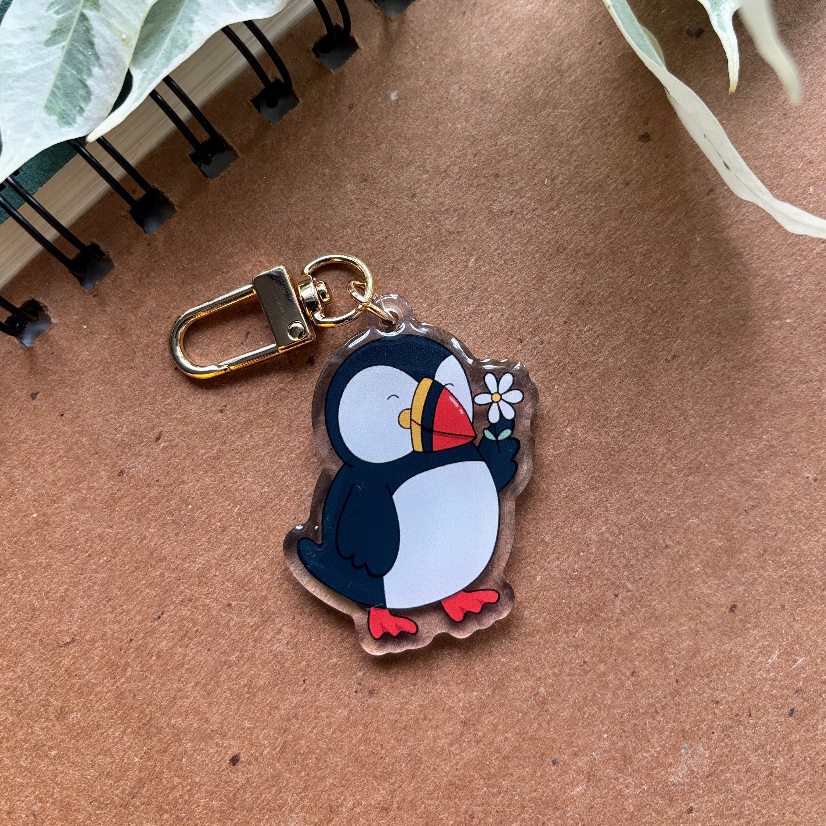 Penguin keychain on a brown surface with green leaves in the background