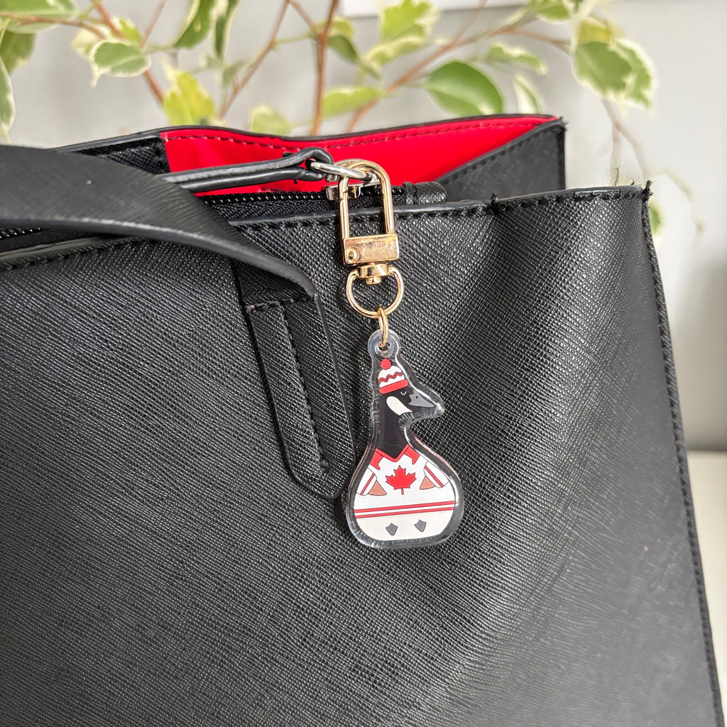 Black handbag with a keychain featuring a canadian goose  design wearing a hockey jacket 