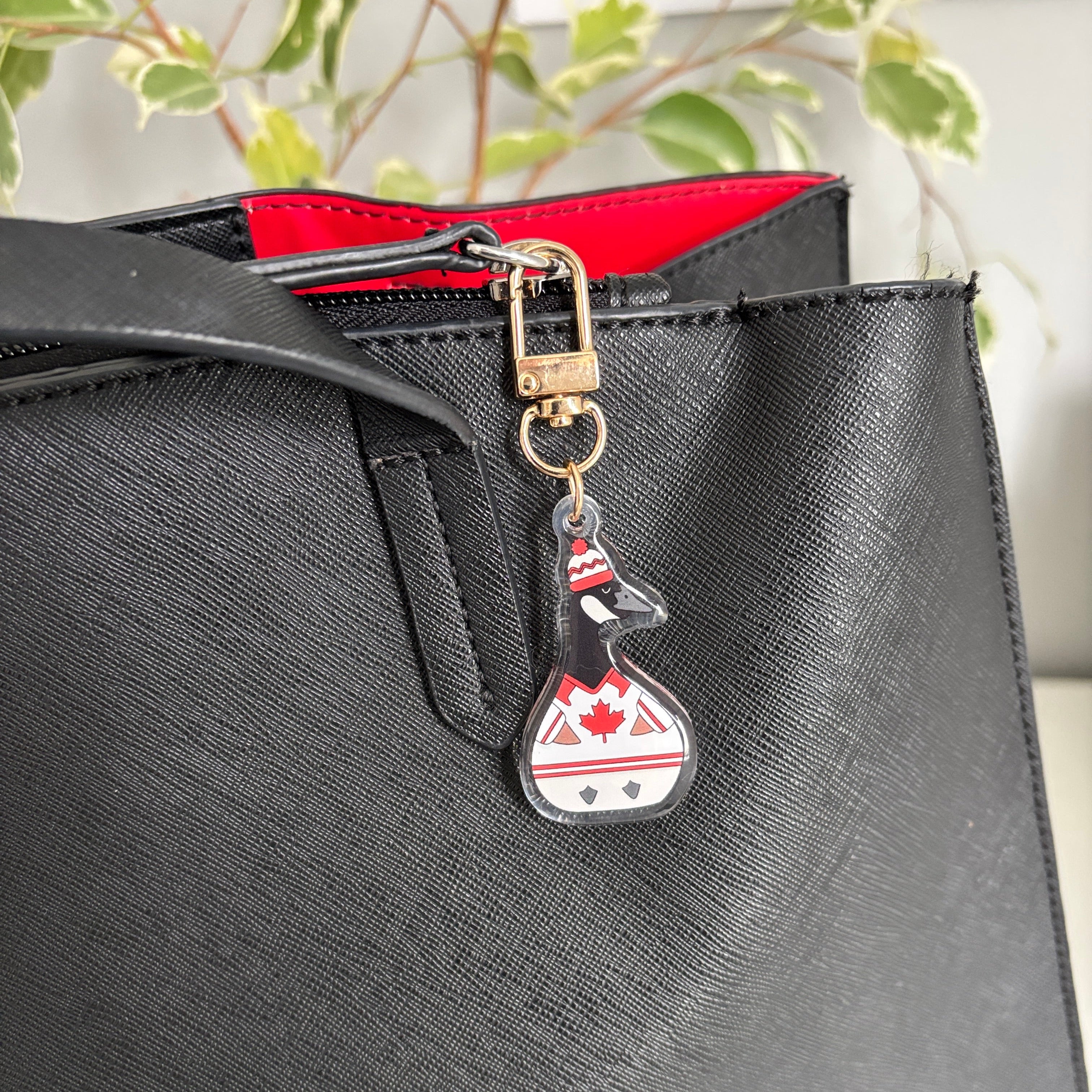 Black handbag with a keychain featuring a canadian goose  design wearing a hockey jacket 
